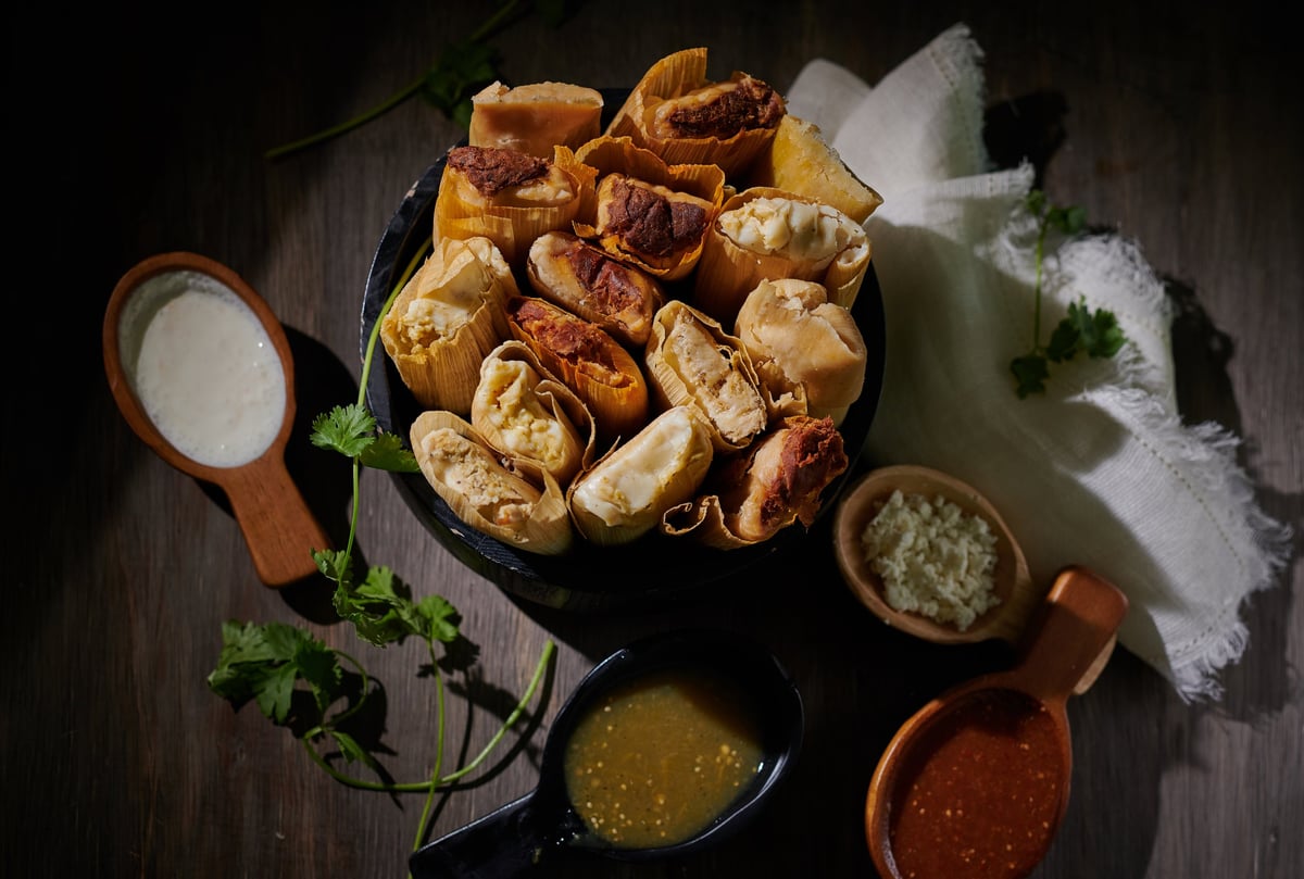 Golden fried empanadas on a black plate with fresh parsley, aioli, and spicy sauce in small bowls on a dark wooden surface