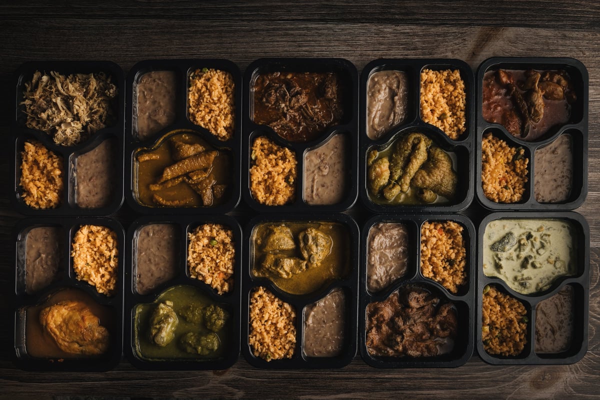 Multiple meal prep containers with assorted foods including breaded proteins, vegetables, and grains arranged on a dark wooden surface