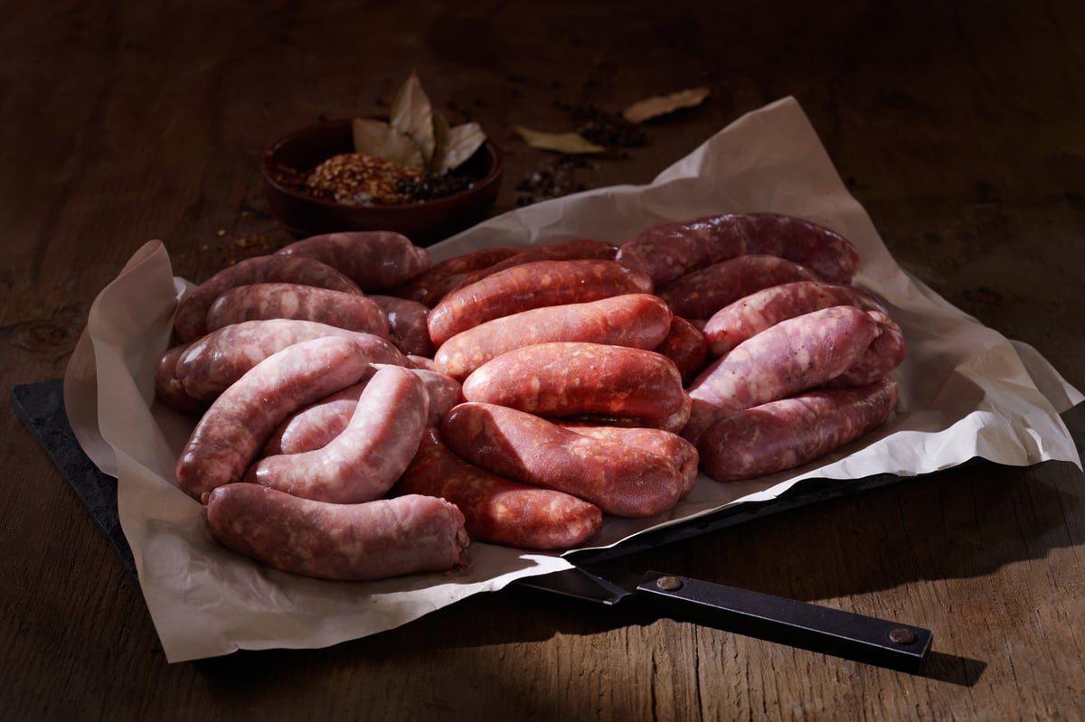 Assorted raw sausages arranged on parchment paper with kitchen shears on a wooden surface