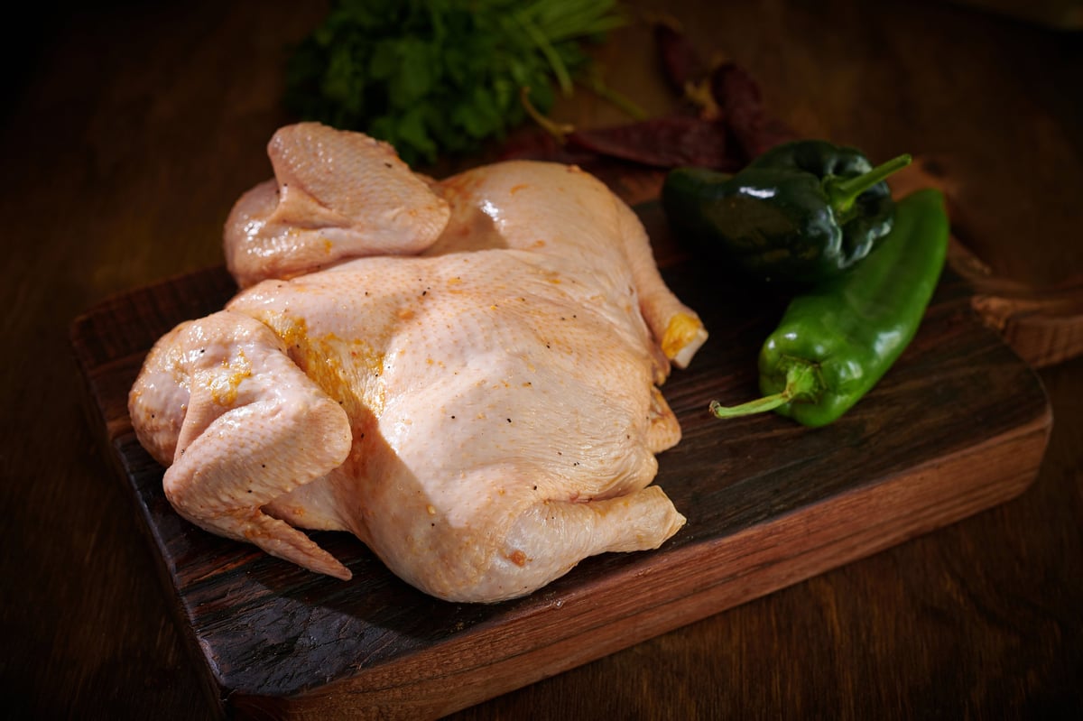 Raw chicken thighs on a wooden cutting board with fresh green peppers and herbs